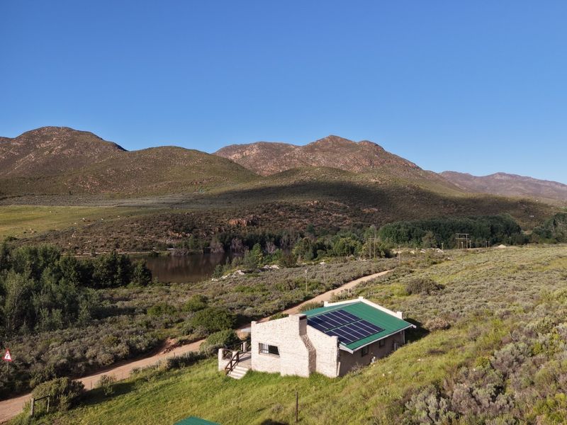 Aerial view of a stone-clad farmhouse featuring a metal roof with integrated solar panels, set within a scenic rural landscape.