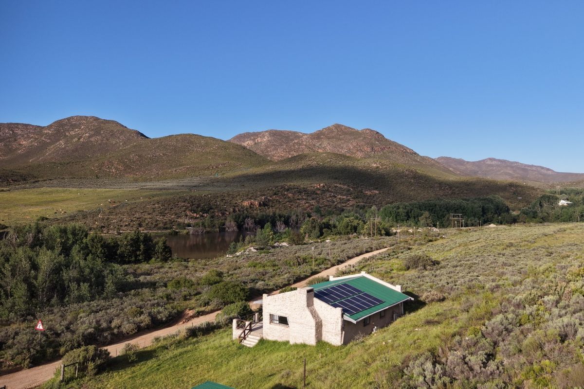 Aerial view of a stone-clad farmhouse featuring a metal roof with integrated solar panels, set within a scenic rural landscape.
