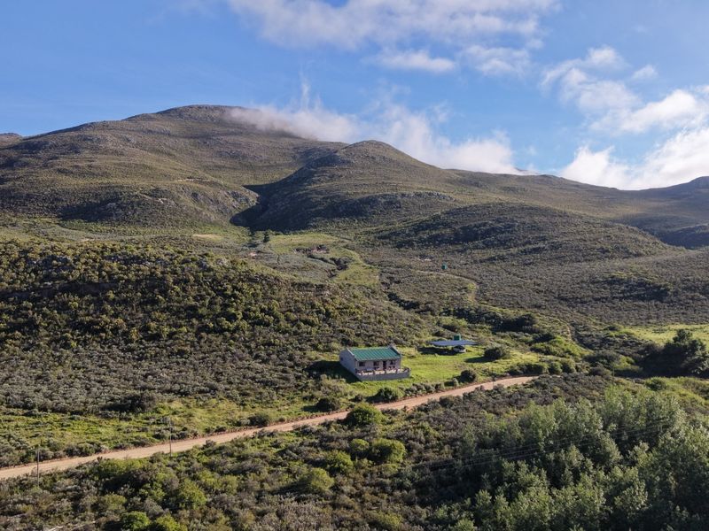 An aerial view of a rural farm property nestled against a large mountain range with a dirt access road.