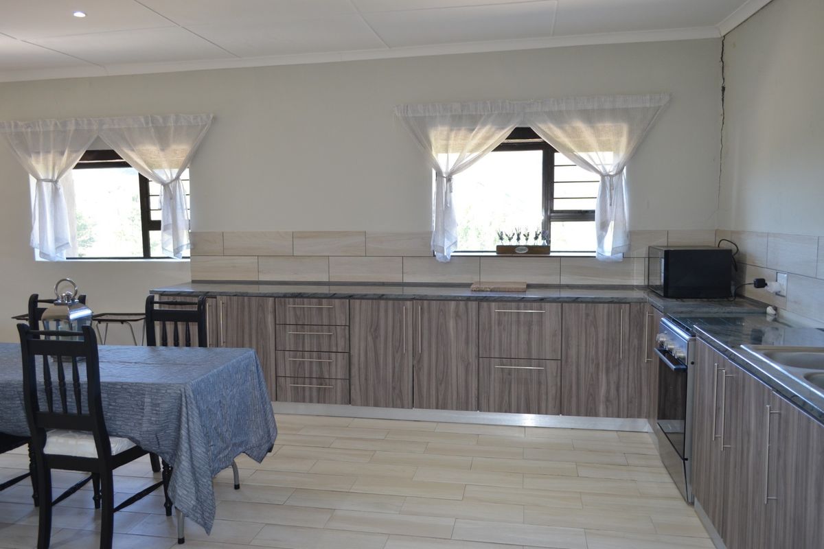 A functional kitchen featuring wood-finish cabinetry, stone countertops, tiled backsplash, and integrated stainless steel appliances, with tiled flooring throughout.