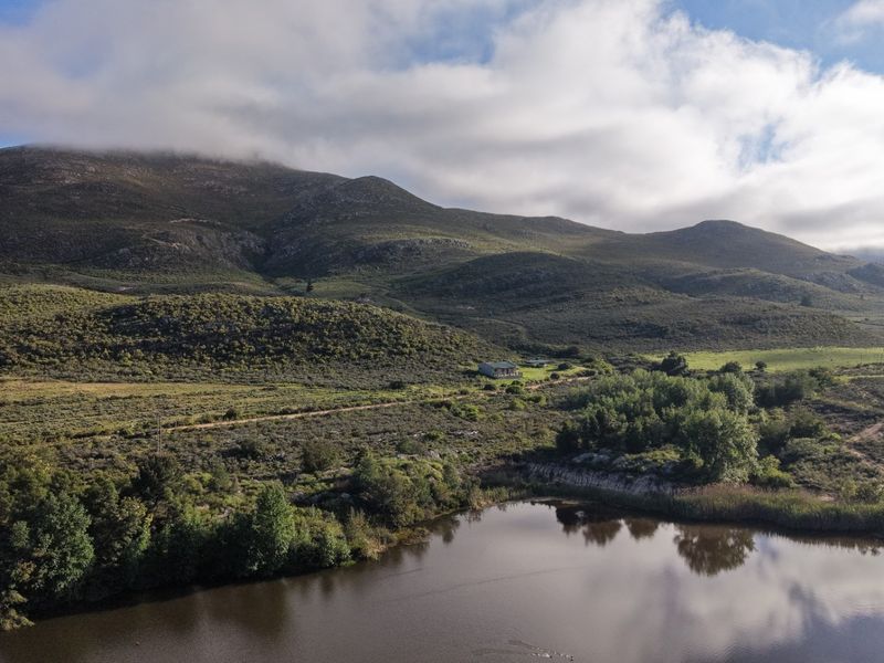 An aerial view of the farm property featuring a large dam, expansive natural landscape, and mountain backdrop.