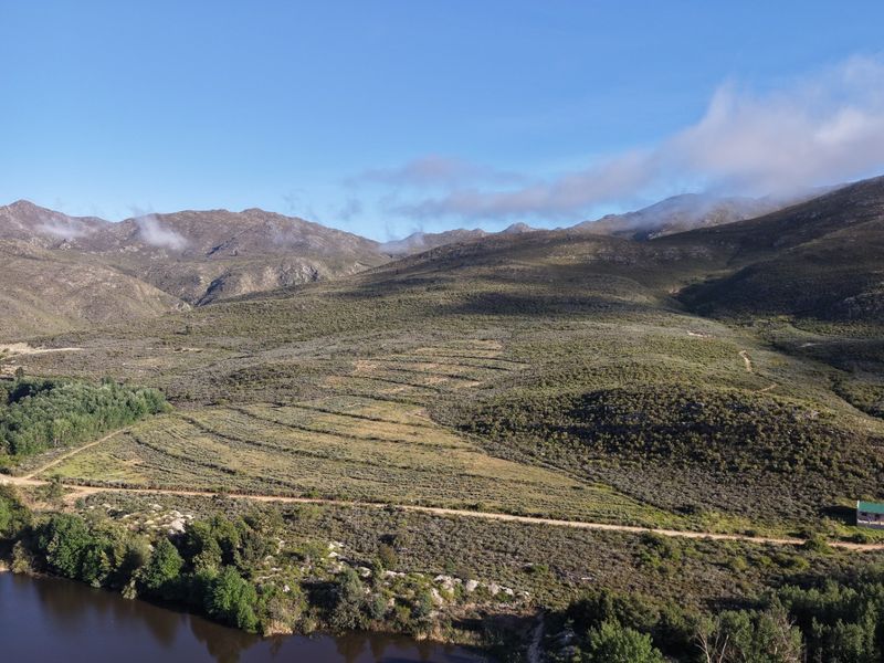 An expansive aerial view of the farm property featuring rolling hills, natural mountain landscape, a river, and a dirt access road.