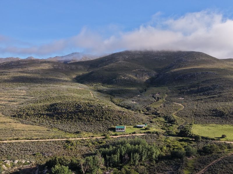 An aerial view of a rural farm property nestled against a large mountain range with expansive natural landscape and access roads.