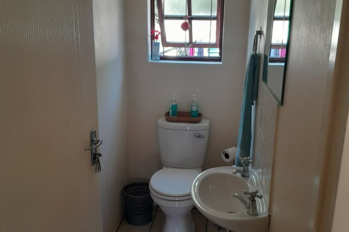 A compact guest bathroom featuring a wall-mounted basin, toilet, and tiled flooring, providing essential utility in a functional layout.