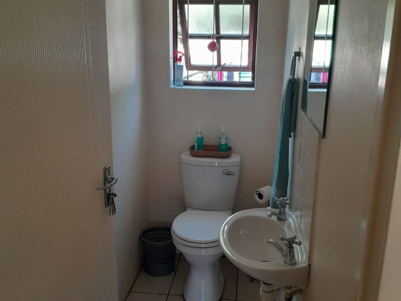 A compact guest bathroom featuring a wall-mounted basin, toilet, and tiled flooring, providing essential utility in a functional layout.