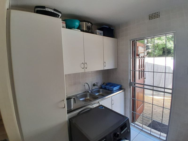 A functional laundry area featuring built-in cabinetry, a stainless steel double sink, and direct access to the exterior through a security gate.