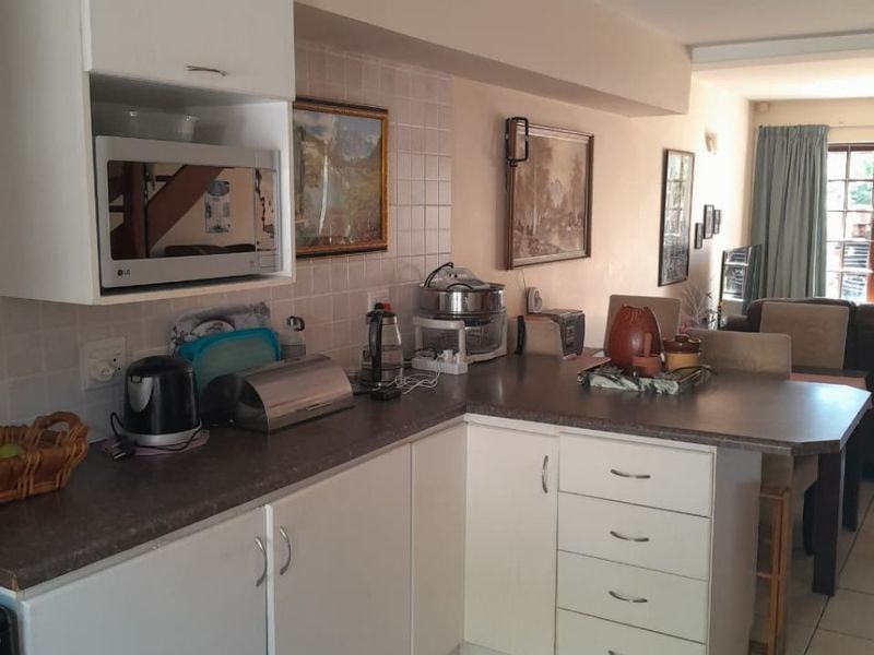 Open plan kitchen featuring white cabinetry, laminate countertops, and tiled flooring, flowing into a connected living area.