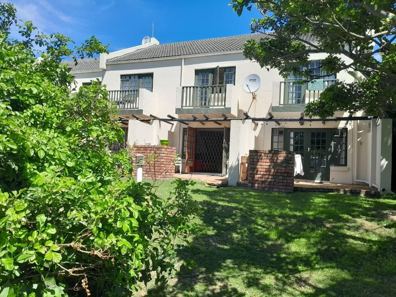 Rear view of the property featuring a private garden, brick-walled patio area, timber pergola, and upper-level balconies with french doors.