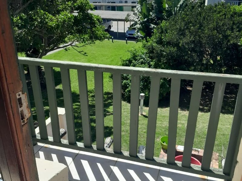 A balcony with tiled flooring and a timber balustrade overlooking a communal garden area.