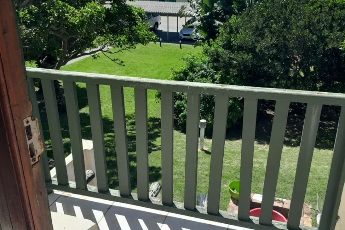 A balcony with tiled flooring and a timber balustrade overlooking a communal garden area.