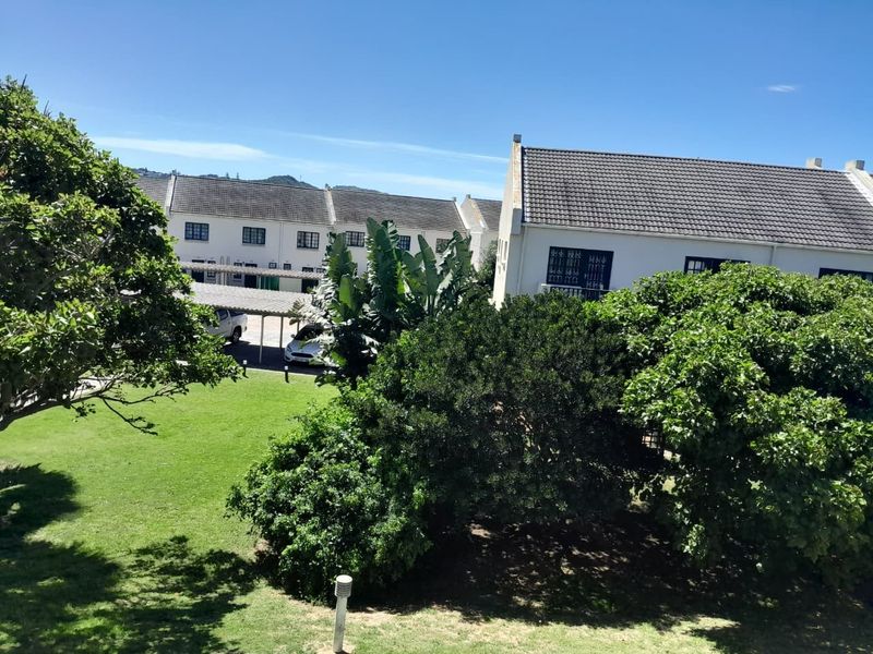 A view of the rear exterior of the property, featuring a well-maintained garden, mature trees, and a covered carport area.