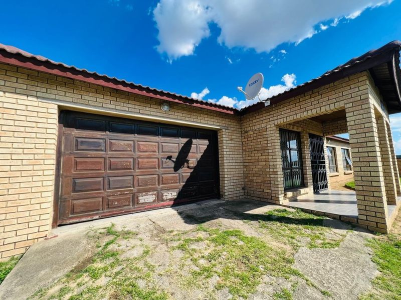 Front exterior view of a brick house featuring a garage, tiled roof, and a paved entrance area with security gate.