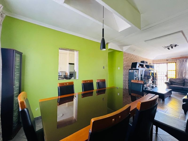 Open-plan dining and living area featuring a brick accent wall, tiled flooring, and a serving hatch connecting to the kitchen.