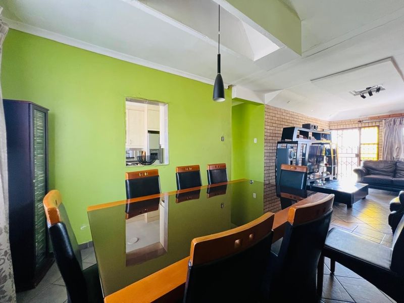 Open-plan dining and living area featuring a brick accent wall, tiled flooring, and a convenient pass-through window connecting to the kitchen.