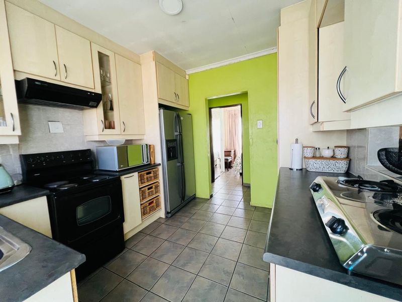 A functional kitchen featuring built-in cabinetry, dark countertops, a built-in oven, and a hob, with tiled flooring and direct access to the living area.