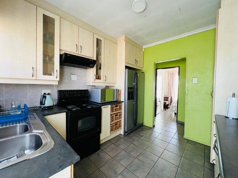 A functional kitchen featuring built-in cabinetry, a double basin sink, and an electric stove, with tiled flooring and a bright green accent wall.