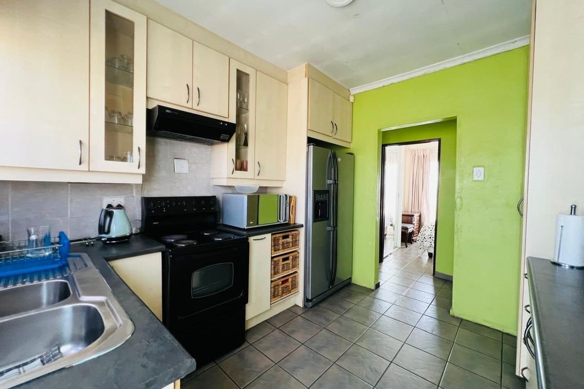 A functional kitchen featuring built-in cabinetry, a double basin sink, and an electric stove, with tiled flooring and a bright green accent wall.