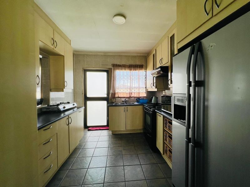 A functional galley-style kitchen featuring laminate cabinetry, dark countertops, tiled flooring, and integrated appliances with direct access to the exterior.