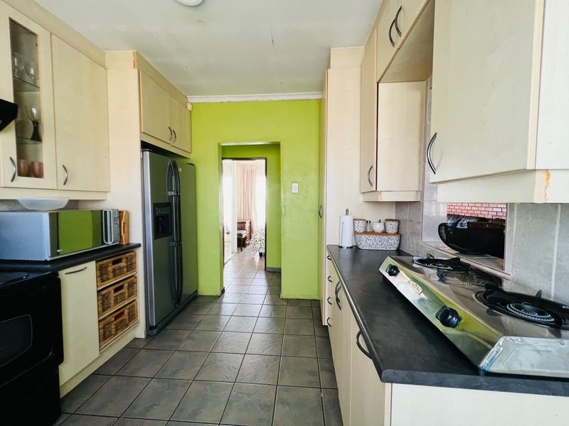 A galley-style kitchen featuring built-in cabinetry, dark laminate countertops, and a gas hob, with tiled flooring and direct access to the adjacent living area.