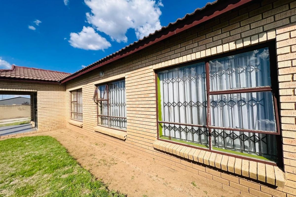 Rear view of a face brick house featuring tiled roofing, metal window frames with security gates, and access to a covered patio area.