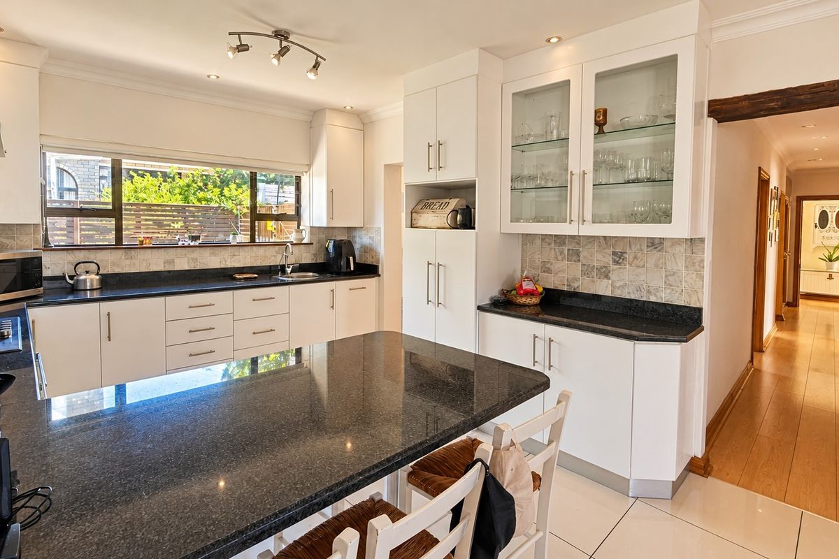Modern kitchen featuring white cabinetry, dark granite countertops, a central island, and a tiled backsplash, flowing into a bright hallway.