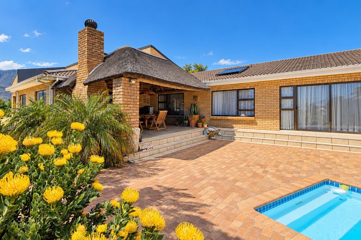 Rear exterior view featuring a paved patio area, swimming pool, and a thatched roof section with brick facade.