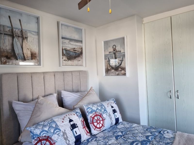 A cozy bedroom featuring a built-in wardrobe and a ceiling fan, decorated with a nautical theme.