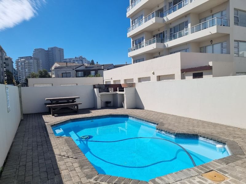 Outdoor pool area featuring a paved deck, built-in braai facility, and surrounding boundary walls, set within a residential apartment complex.