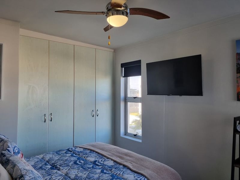 A well-maintained bedroom featuring built-in cupboards, a ceiling fan, and a window with a roller blind.