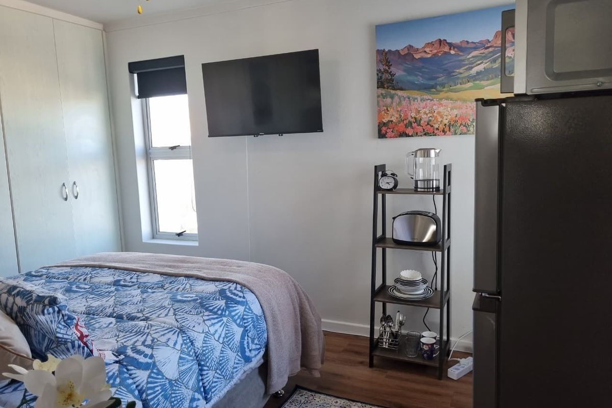 A functional bedroom featuring built-in wardrobe storage, laminate flooring, and a wall-mounted television.