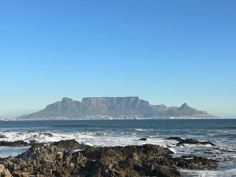 A scenic coastal view overlooking rocky shoreline with Table Mountain visible in the distance.