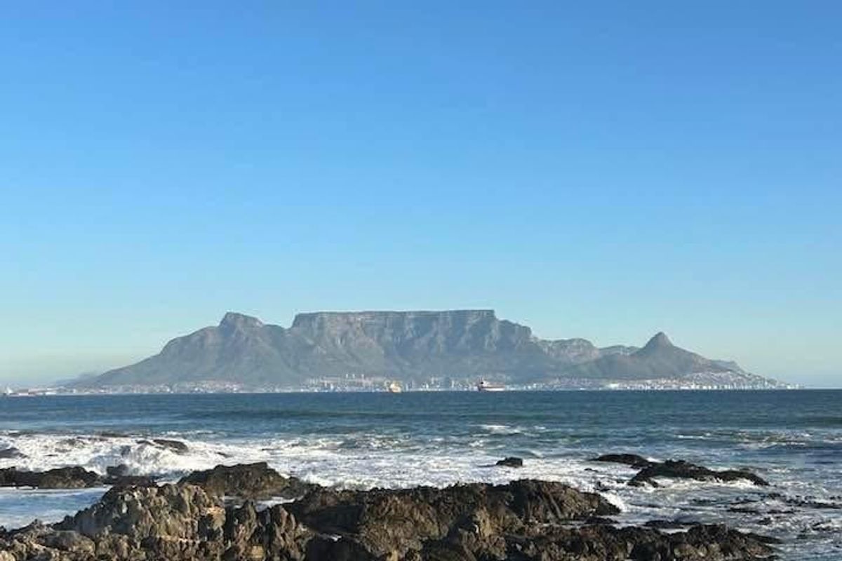 A scenic coastal view overlooking rocky shoreline with Table Mountain visible in the distance.