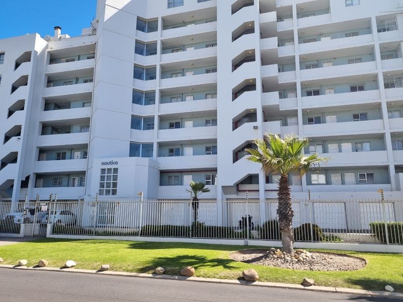 Front exterior view of the Nautica apartment complex, featuring a multi-story building with secure perimeter fencing and well-maintained landscaped grounds.