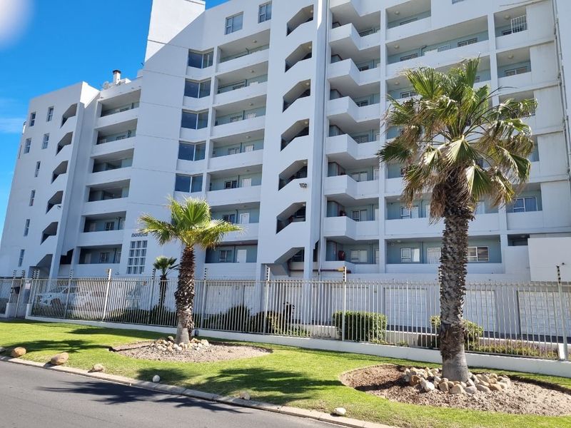 Exterior view of a multi-story apartment complex featuring private balconies, secure perimeter fencing, and well-maintained landscaped grounds.