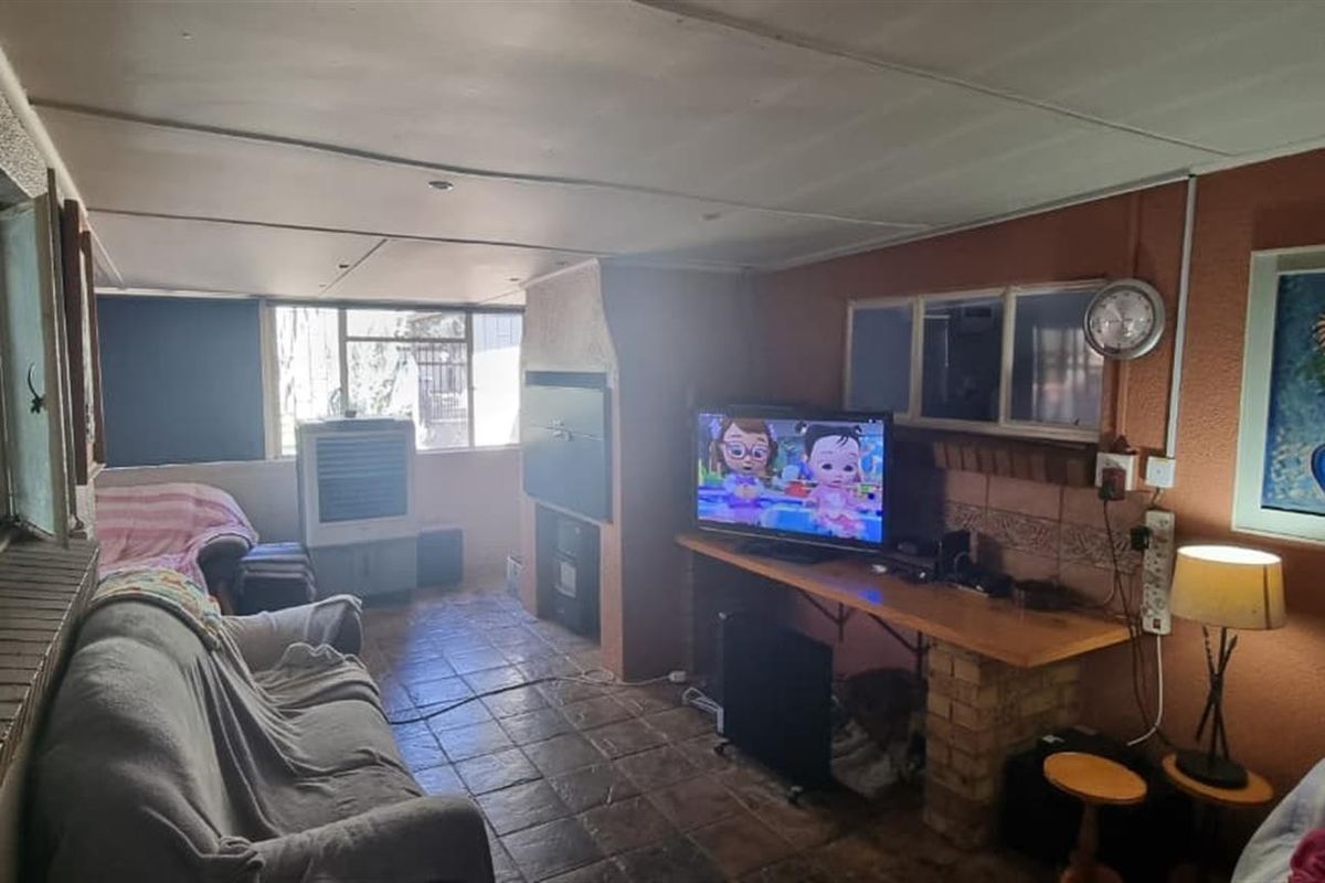 A living room featuring tiled flooring, a built-in fireplace, and brick-based shelving, offering a functional space with potential for cosmetic updates.