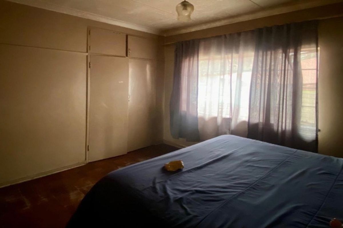 A bedroom featuring built-in cupboards and natural light from a window, requiring cosmetic updates to the flooring and wall finishes.