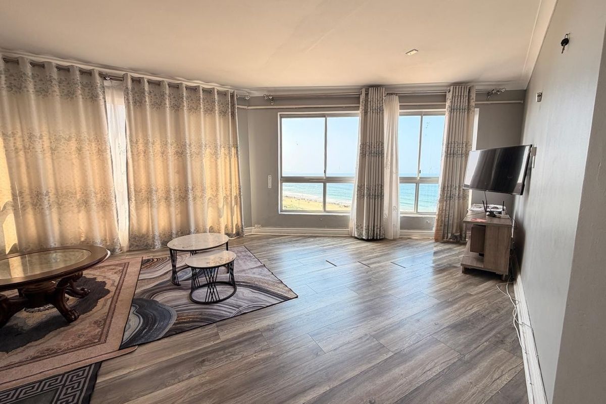 Spacious living room featuring wood-look laminate flooring and large windows offering direct ocean views, providing a bright and airy atmosphere.