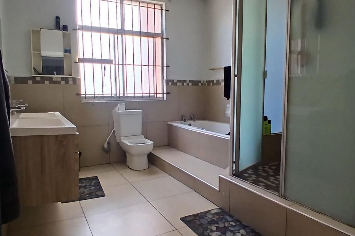 A functional bathroom featuring a built-in vanity, toilet, bathtub, and a separate shower enclosure with tiled finishes and security bars on the window.