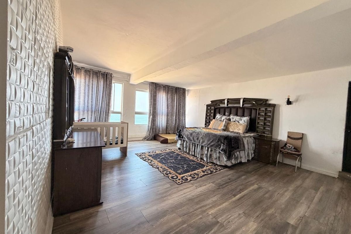 Spacious bedroom featuring wood-look laminate flooring, textured feature wall, and large windows providing natural light.