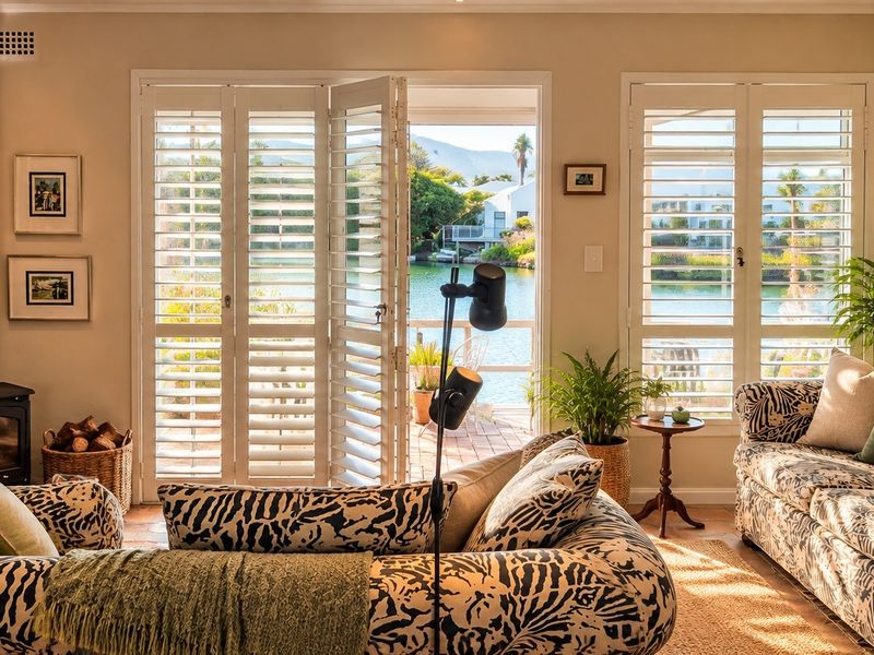 Cozy living room featuring a wood-burning stove, terracotta flooring, and plantation shutters opening onto a scenic waterfront patio.