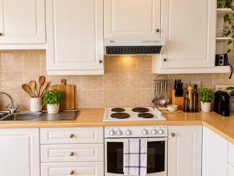 A well-maintained kitchen featuring white shaker-style cabinetry, a light wood-tone laminate countertop, a stainless steel sink, and a built-in electric oven and hob.