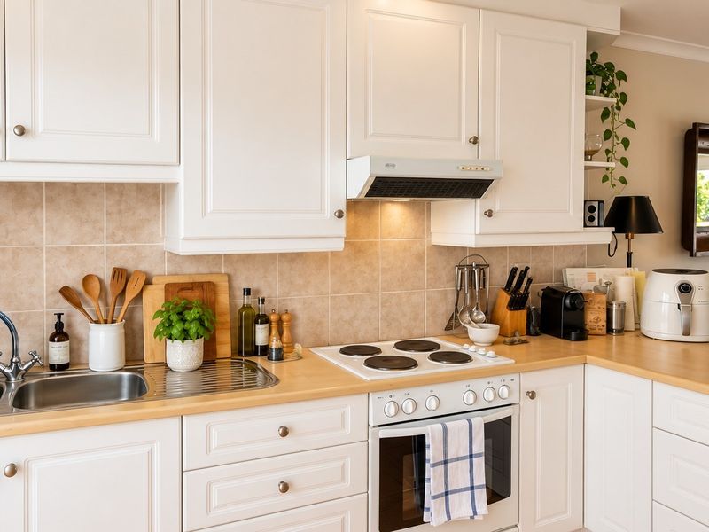 A well-maintained kitchen featuring white shaker cabinetry, light wood-look laminate countertops, a ceramic hob, and a tiled backsplash.
