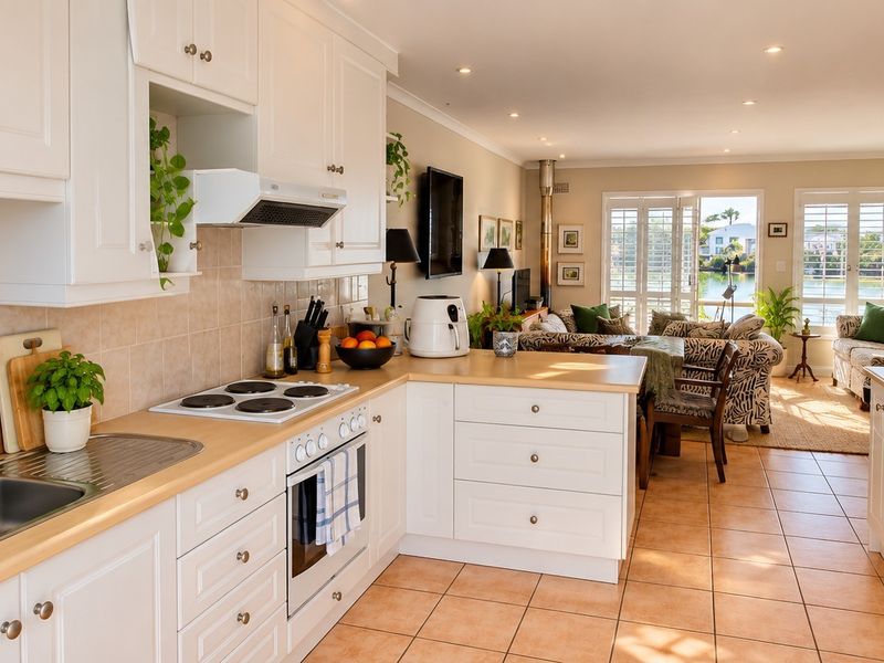 Spacious open-plan kitchen and living area featuring white cabinetry, tiled flooring, and direct access to a patio with water views.