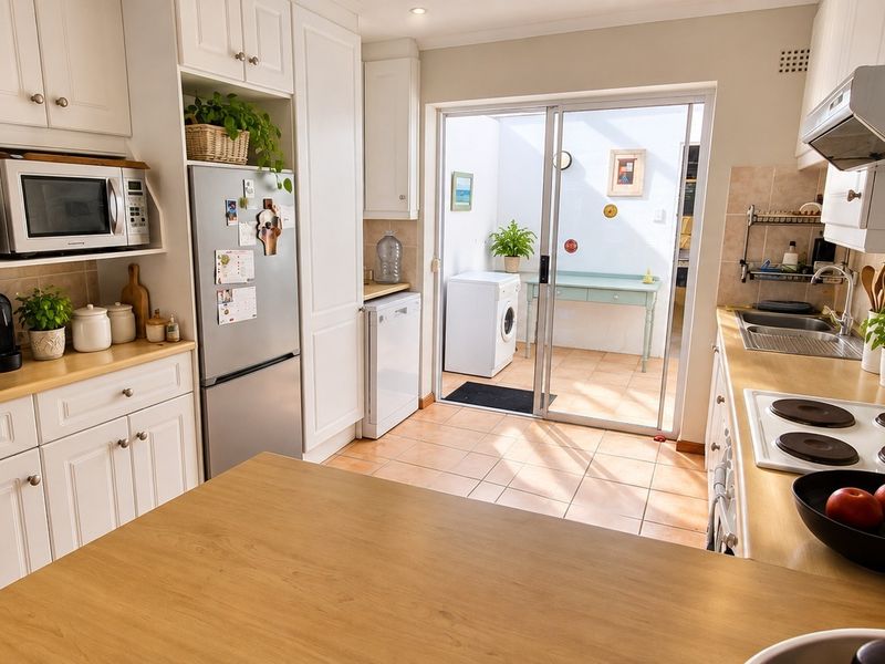 A well-maintained kitchen featuring white cabinetry, laminate countertops, an electric hob with extractor, and direct access to an outdoor patio area.
