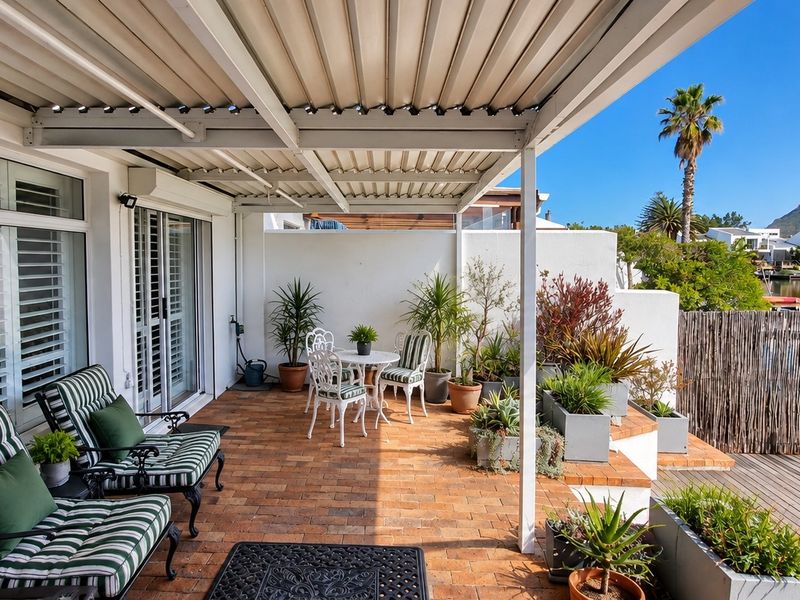 A covered patio featuring brick paving and a louvre roof, offering direct access to the water with scenic views.