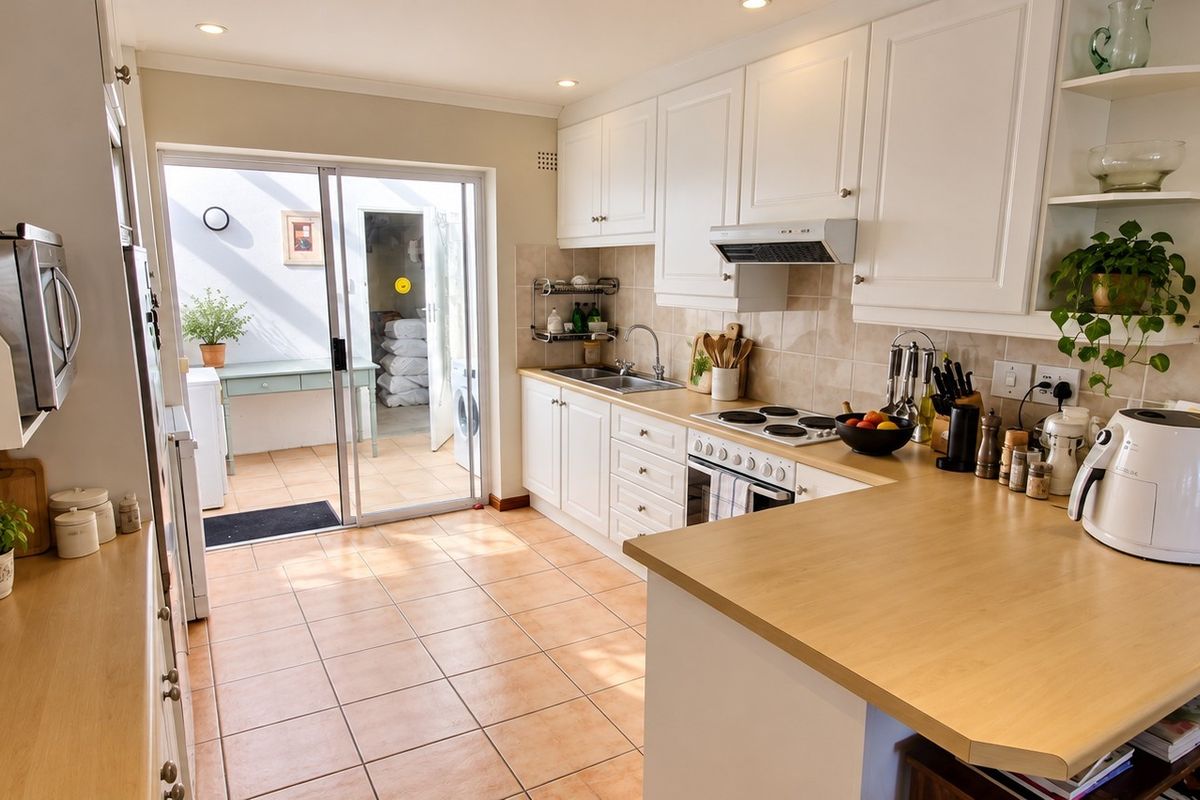 A well-maintained kitchen featuring white cabinetry, light wood countertops, an electric hob, and direct access to an outdoor patio area through sliding doors.