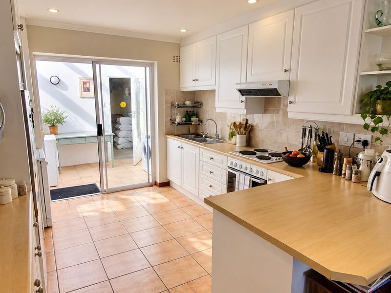 A well-maintained kitchen featuring white cabinetry, light wood countertops, an electric hob, and direct access to an outdoor patio area through sliding doors.