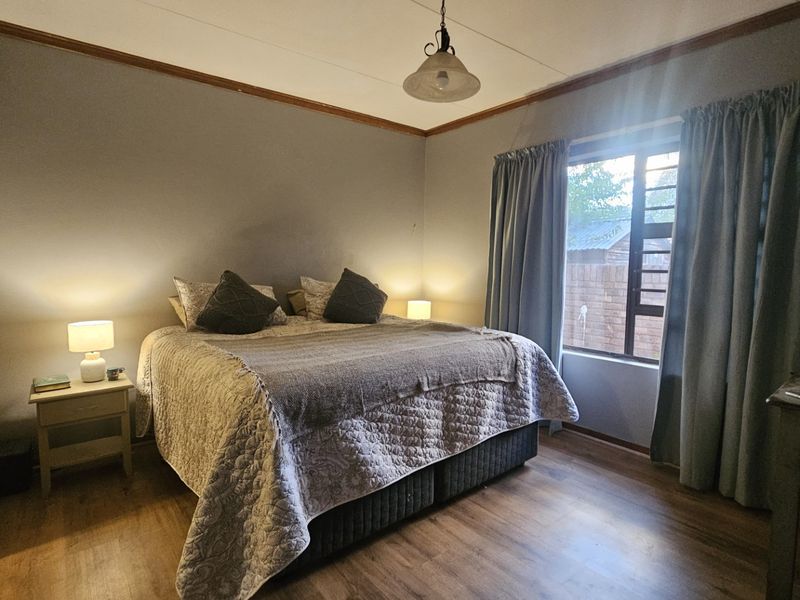 A comfortable bedroom featuring laminate flooring, timber crown molding, and a window with security bars, providing a functional and well-lit sleeping space.