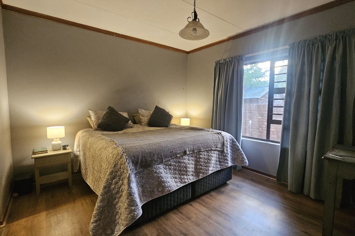 A comfortable bedroom featuring laminate flooring, timber crown molding, and a window with security bars, providing a functional and well-lit sleeping space.