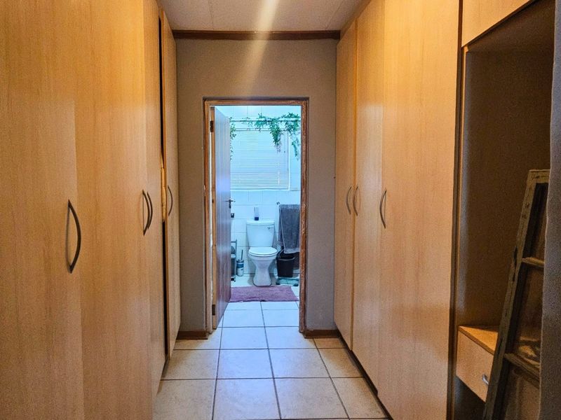 A hallway featuring extensive built-in wooden cupboards and tiled flooring, providing direct access to an adjacent bathroom.
